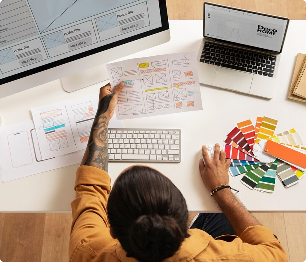 Overhead view of a designer’s desk with color swatches, laptop, and wireframe sketches