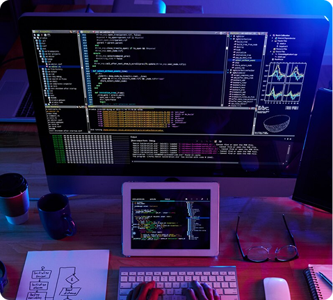 Monitor and laptop displaying UI design and code in a dark workspace